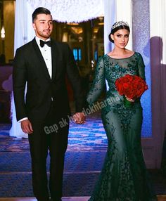 a man and woman dressed in formal wear holding hands while walking down a hall with chandeliers