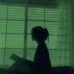 a person sitting on a bed with a book in front of them and blinds behind them