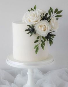 there is a white cake with flowers on the top and green leaves on the bottom