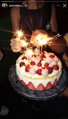 a cake with strawberries and sparklers on it is being held by a woman