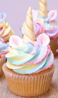 cupcakes with frosting and unicorn ears on them sitting on a wooden table