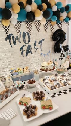 a table topped with lots of desserts next to a wall covered in black and white balloons