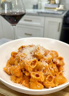 a white bowl filled with pasta next to a glass of wine