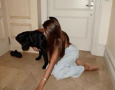 a woman sitting on the floor petting a black dog's head and nose