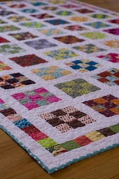 a close up of a quilt on a wooden table with a wood floor in the background