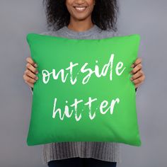 a woman holding a green pillow with the words outside hitter printed on it in white