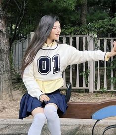 a woman sitting on top of a bench next to a wooden park bench and holding her hand out