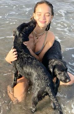 a woman sitting in the water with two dogs on her lap, both holding each other