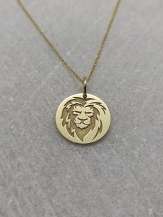 a gold necklace with a lion head on it's front and back sides, sitting on a gray surface