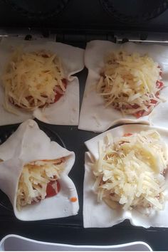 four pizzas are wrapped in paper and ready to go into the oven with cheese