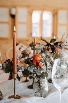 a table with candles and flowers in vases on it's centerpiece, along with other place settings