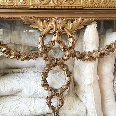 an ornately decorated gold framed mirror on display in a room with white linens