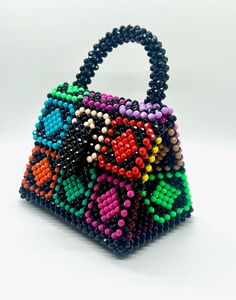 This small bag packs a big hit of style and glamour with it's glistening, hand woven beads. Handmade in Argentina, this micro bag has vibrant pops of diamond shaped color against it's back bag. Although stunningly beautiful, it is not without flexibility as the triangle shape expands to hold all your goodies. Bag comes with insert as well. Plastic beads 6.25" L x 4.5" W x 8" H Multicolor Top Handle Bag As Gift, Multicolor Top Handle Bag For Gift, Multicolor Beaded Pouch Bag, Multicolor Beaded Handheld Shoulder Bag, Trendy Multicolor Beaded Shoulder Bag, Multicolor Square Bags, Trendy Multicolor Beaded Bags, Multicolor Rectangular Bag With Colorful Beads, Multicolor Rectangular Shoulder Bag With Colorful Beads