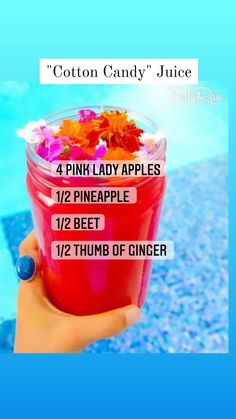 a person holding up a pink lady apple drink in front of a pool with flowers