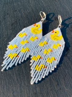 a pair of yellow and white bird earrings on top of a black surface next to each other