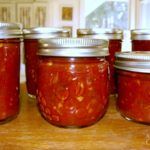 four jars filled with red sauce sitting on top of a wooden table