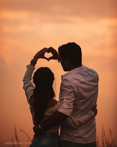 a man and woman making a heart shape with their hands in front of the sunset