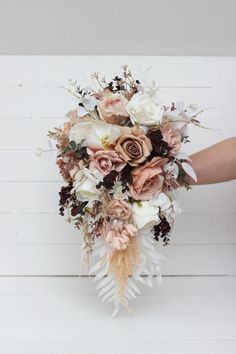 a bridal bouquet is being held in front of a white wooden wall with planks