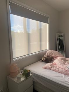 a bed with pink sheets and pillows in a small room next to a large window