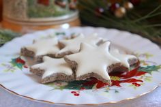 three cookies on a plate with white icing and holly decorations around them, sitting next to a christmas tree