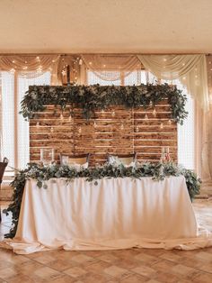 a table is set up with greenery and candles for an elegant wedding reception in front of a wooden paneled wall