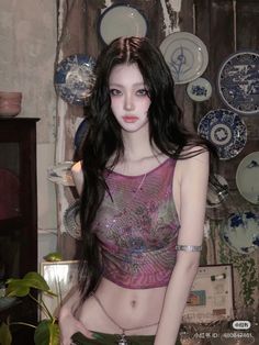 a woman with long black hair is posing in front of plates on the wall behind her