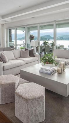 a living room filled with lots of furniture and large windows overlooking the water in the distance