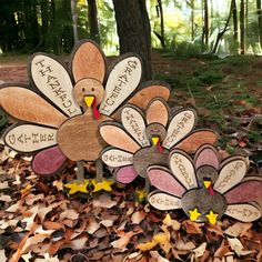 three wooden turkeys sitting on top of leaves next to a tree in the woods