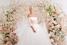 a woman in a white wedding dress standing next to a floral arch with pink flowers