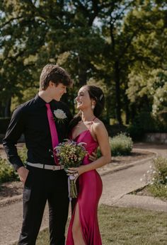 a young man and woman standing next to each other in front of some trees holding flowers