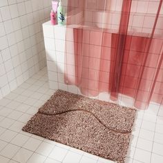 a bath room with a toilet and a rug on the floor in front of a shower