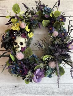 a wreath with flowers and a skull in the middle on a white wooden wall background