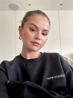 a woman wearing a black sweatshirt with the word rare impact printed on it and gold hoop earrings