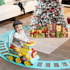 a little boy riding a toy train next to a christmas tree