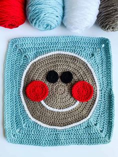 a crocheted square with two balls of yarn next to it and the face of a