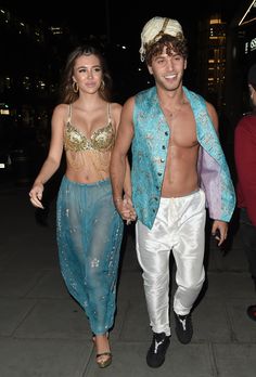 a man and woman walking down the street at night wearing belly dance outfits, with one holding the other's hand