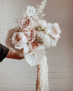 a person holding a bouquet of flowers in front of a brick wall with white and pink colors