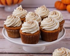 cupcakes with frosting sitting on a white cake plate next to pumpkins