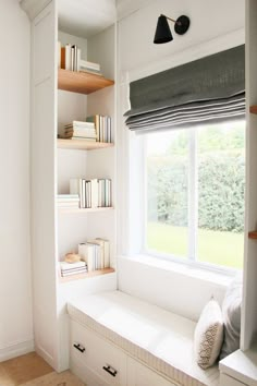 a window seat in front of a book shelf with books on it and a pillow