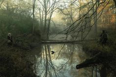 two people are standing near a pond in the woods