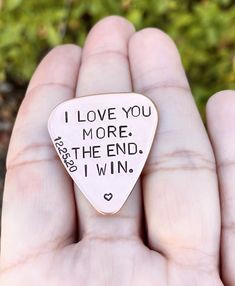 a hand holding a small guitar pick that says i love you more the end i win