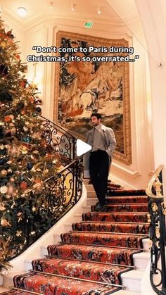 a man is walking down the stairs in front of a christmas tree