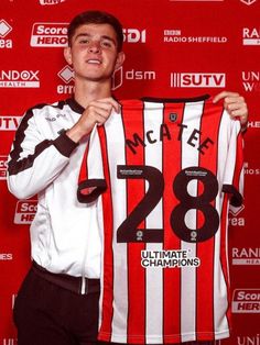 a young man holding up a soccer jersey in front of a red wall with the number 28 on it