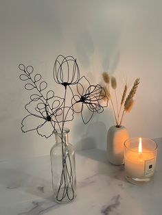 two vases filled with flowers and candles on a marble counter top next to each other