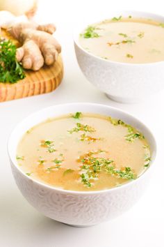 two white bowls filled with soup next to some bread and garlic on a table top