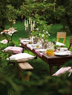 an outdoor table set with plates and glasses on it in the middle of a grassy area