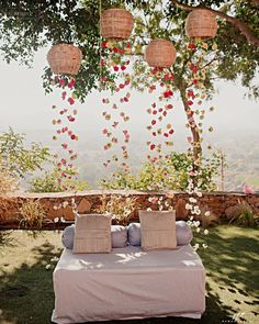 a bed sitting under a tree next to a lush green hillside covered in pink flowers