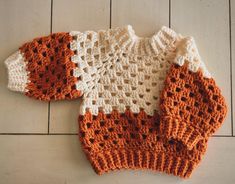 an orange and white knitted sweater laying on the floor