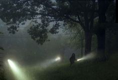 two people are walking in the dark with lights shining on their bodies and trees behind them