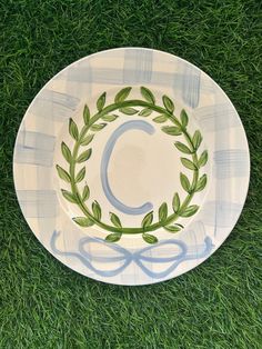 a white plate with green leaves and a letter c on it sitting in the grass